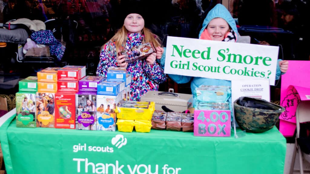2 Girl Scouts selling cookies outside. 