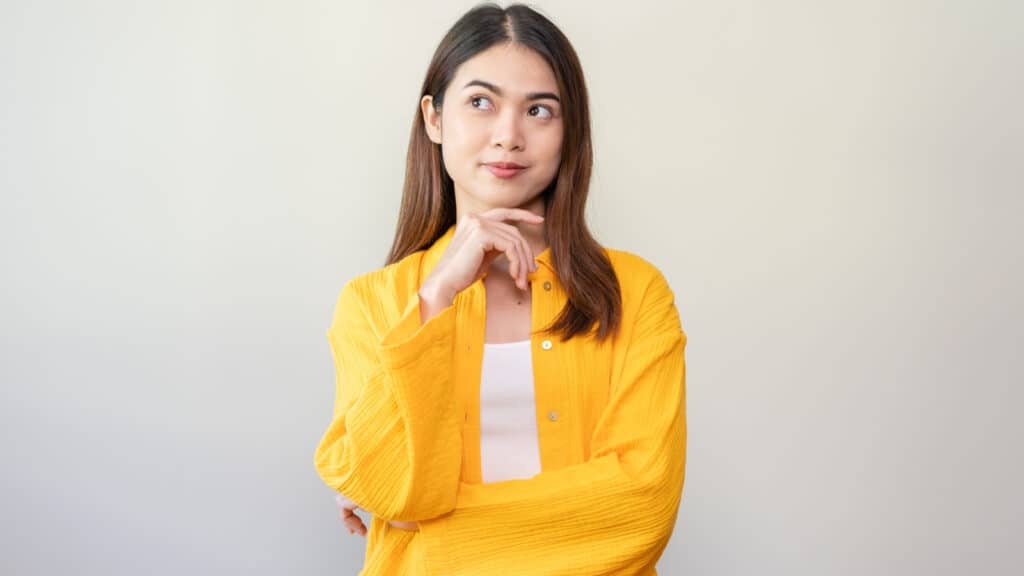 Asian woman with long hair in yellow shirt thinking. Wondering.