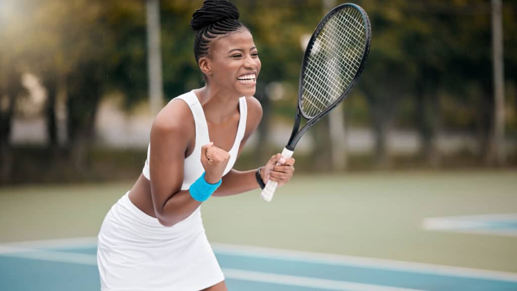 Black woman playing tennis in tennis whites.