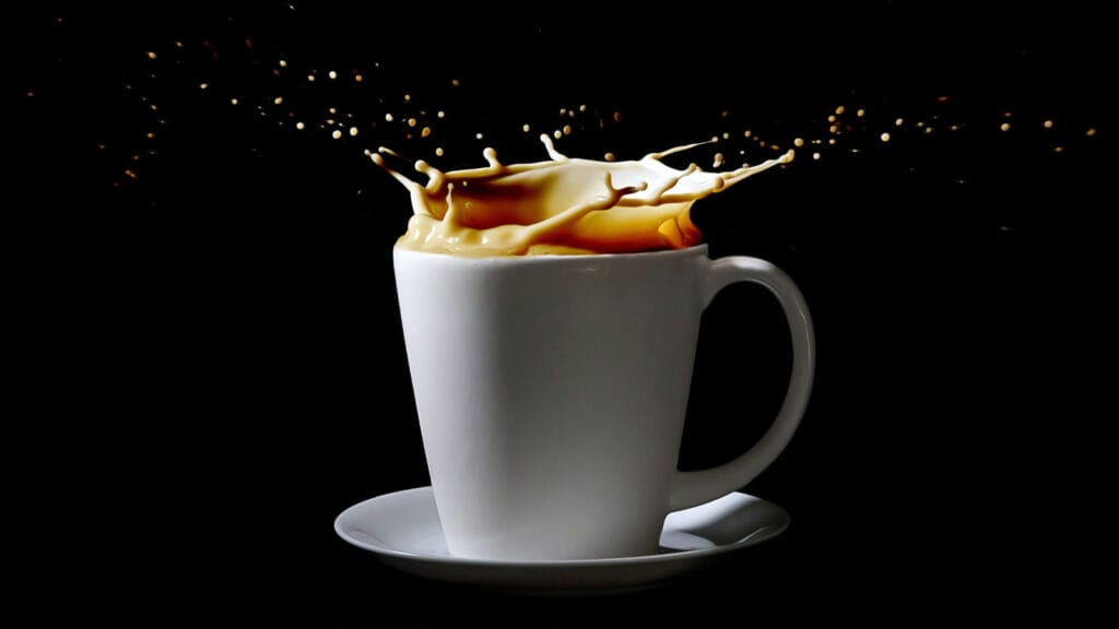 Cup of coffee in white mug. Coffee and milk splashing out of top of cup. Milk splash.