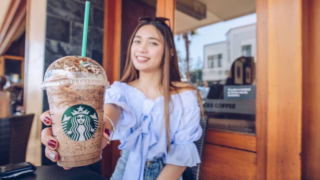 young woman with long hair holding blended Starbucks drink.