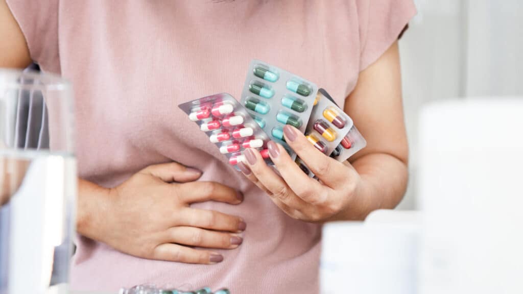 woman holding several packages of blister pack pills. Antibiotics. Not good for your gut health. 
