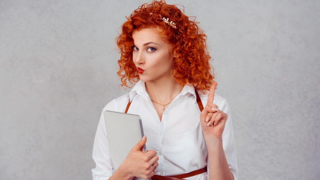 Curly red haired woman in white shirt wagging finger.