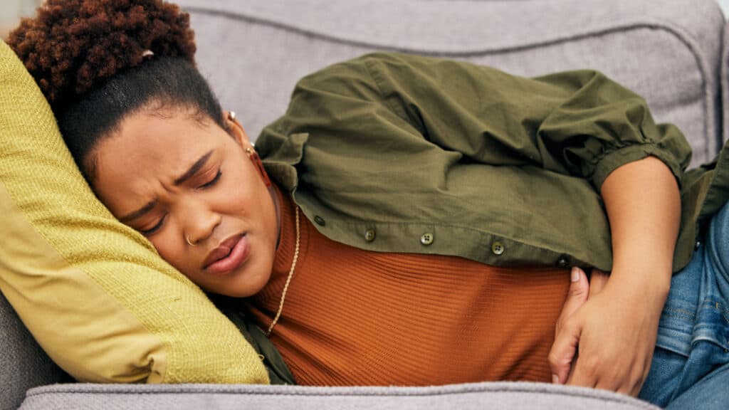 African American woman holding stomach lying on couch in pain.