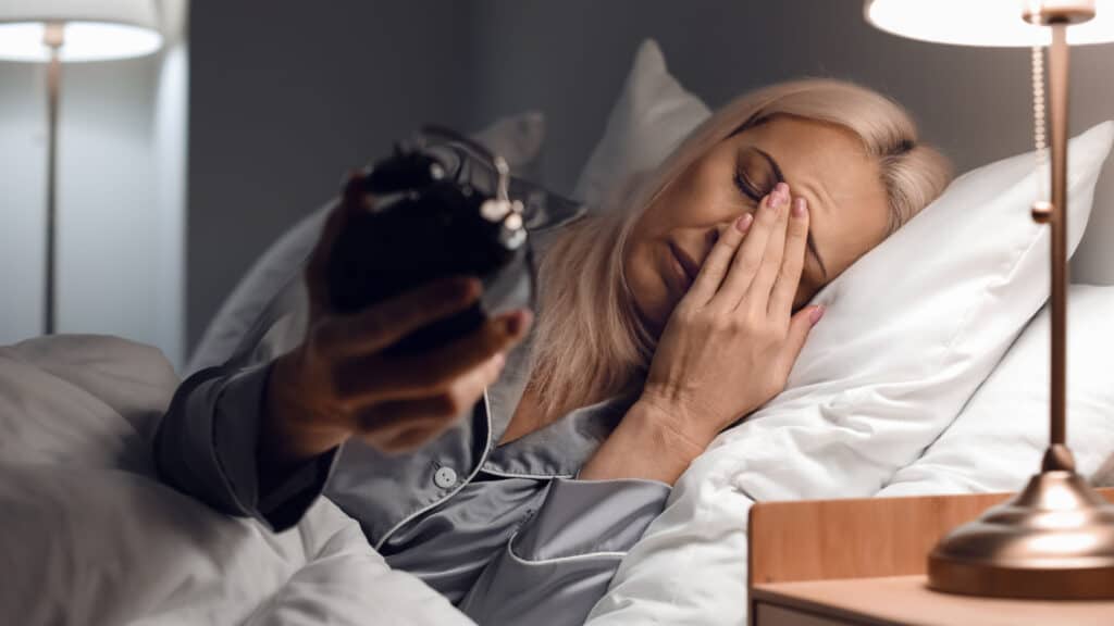 blonde woman in bed with insomnia looking at clock.