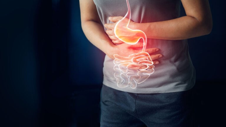 person in gray T shirt holding stomach. Belly ache. Stomach ache.