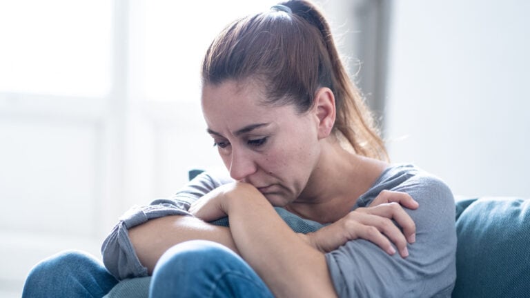 Woman with ponytail sitting on floor, clutching knees, looking depressed. Depressed woman. Sad woman.