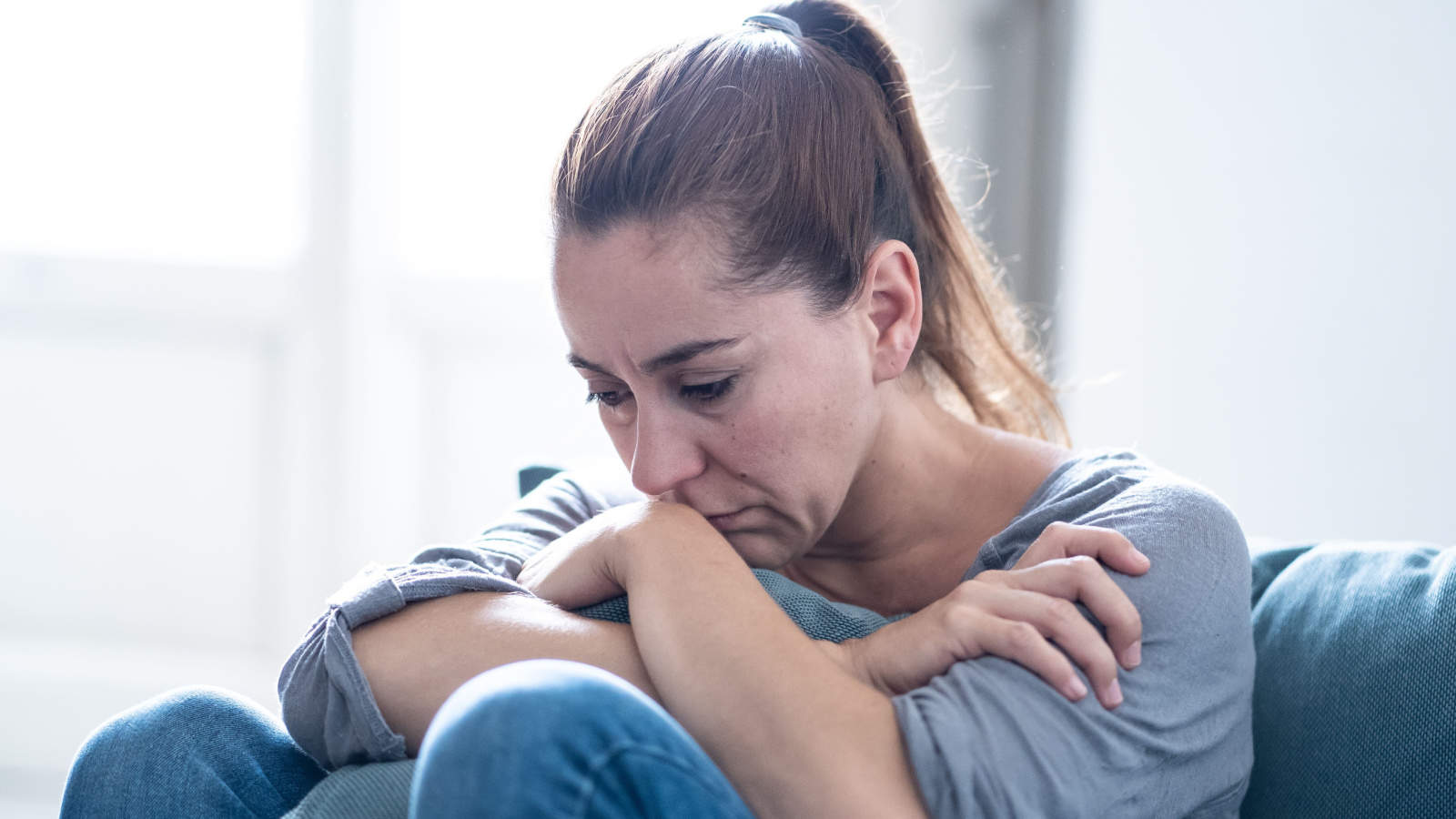 Woman with ponytail sitting on floor, clutching knees, looking depressed. Depressed woman. Sad woman.