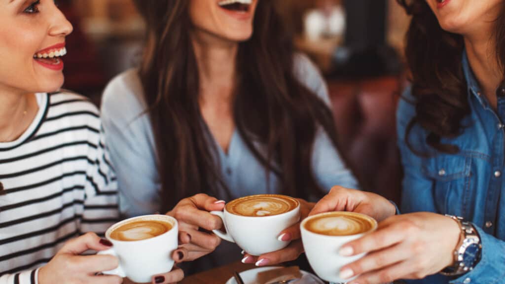 Three young women in coffee shop drinking coffee and laughing.