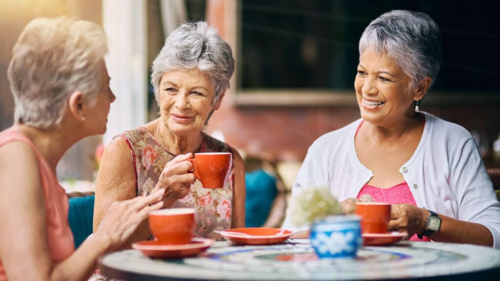 Three older senior women with grey hair drinking coffee.