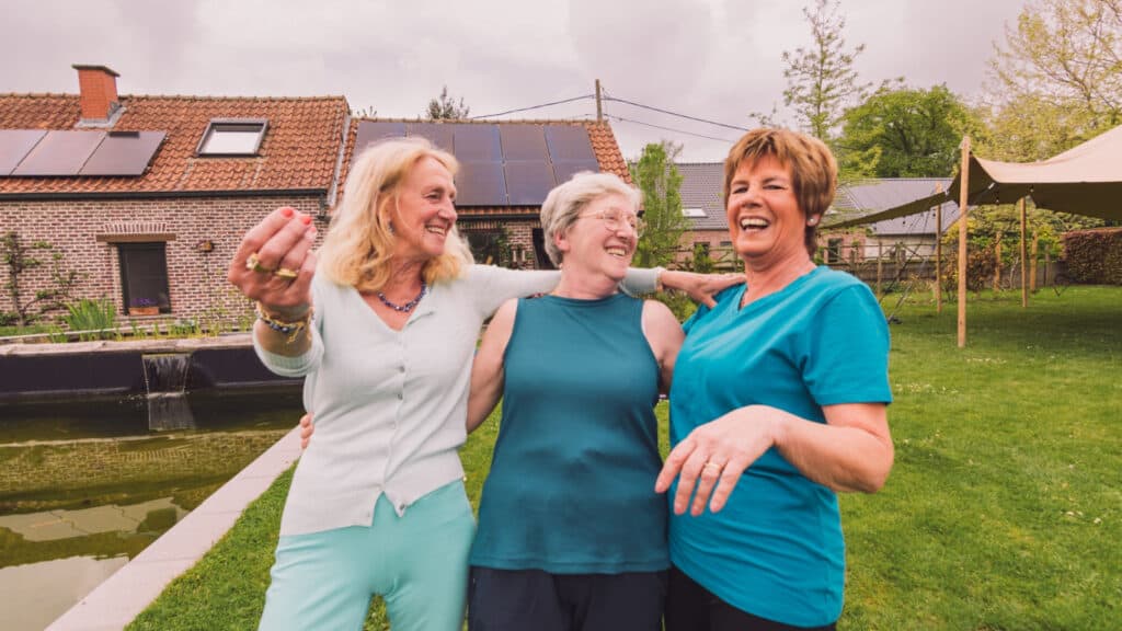 Three older women outside in a courtyard amongst suburban houses.