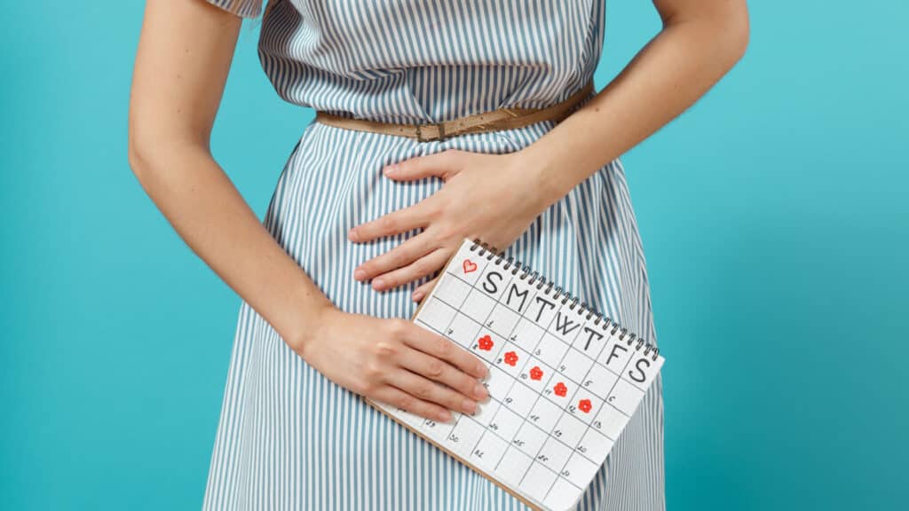 Woman clutching stomach holding calendar showing period days. IBS 