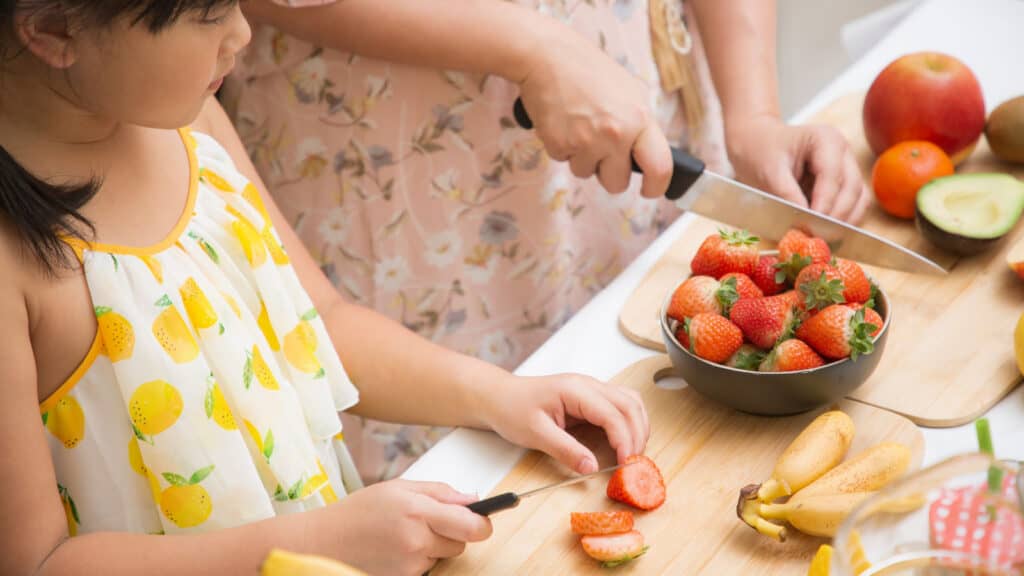 Adult making fruit salad with little girl.