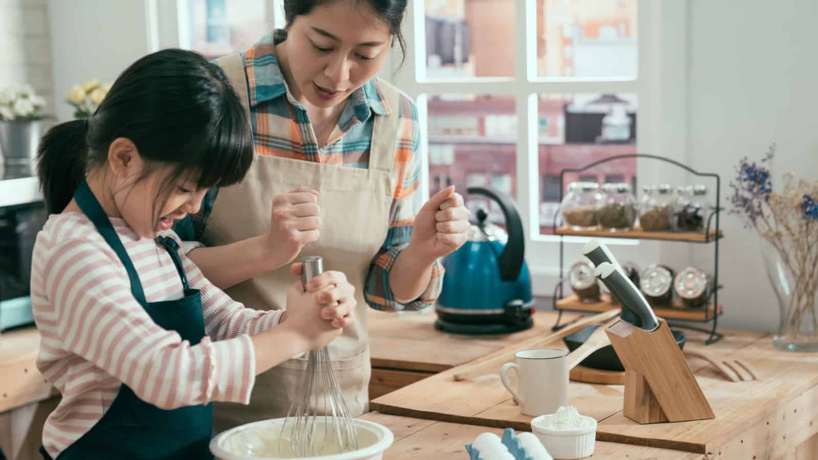 Asian mom and child whisking ingredients in bowl.
