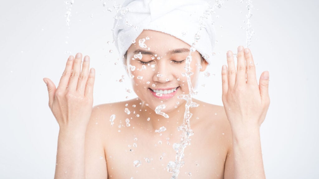 Asian woman splashing face with water.