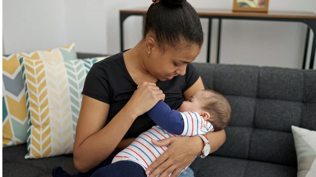 Black African American mother breastfeeding sitting on couch. 