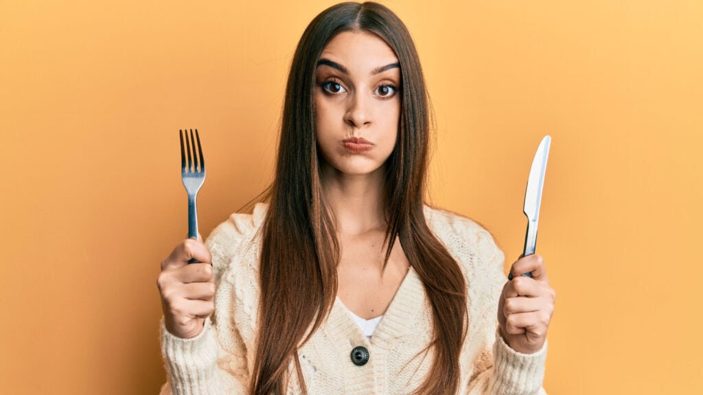 Confused woman holding knife and fork. 