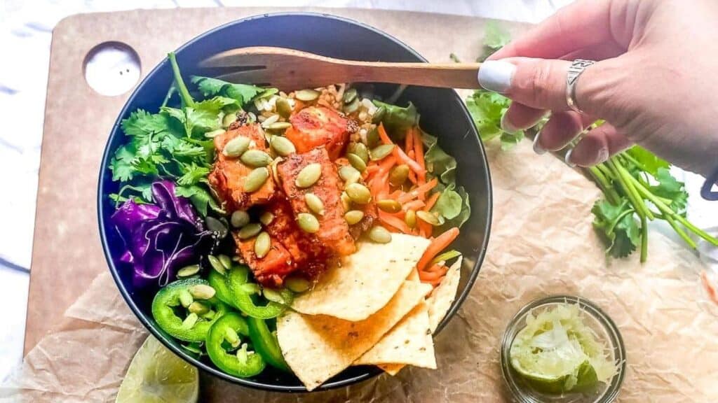 Low-FODMAP-Baja-Tempeh-Taco-Salad-in-dark-bowl-womans-hand-holding-wooden-fork.