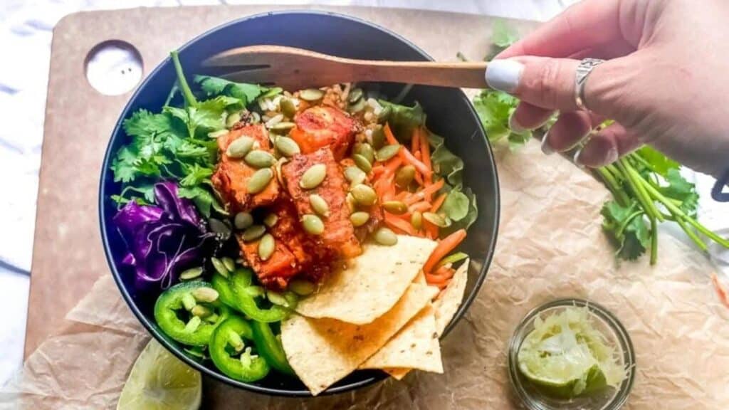 Low-FODMAP-Baja-Tempeh-Taco-Salad-in-dark-bowl-womans-hand-holding-wooden-fork.