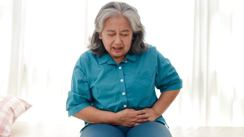 Older Asian woman clutching stomach. IBS pain.