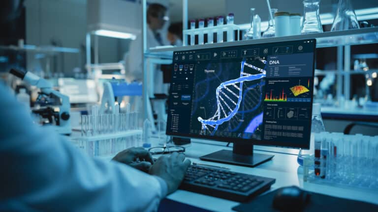 Medical Research Scientist Working on Desktop Computer with Gene Analysis Software in Modern Science Research Laboratory. Lab Engineers in White Coats Conduct Experiments in the Background.