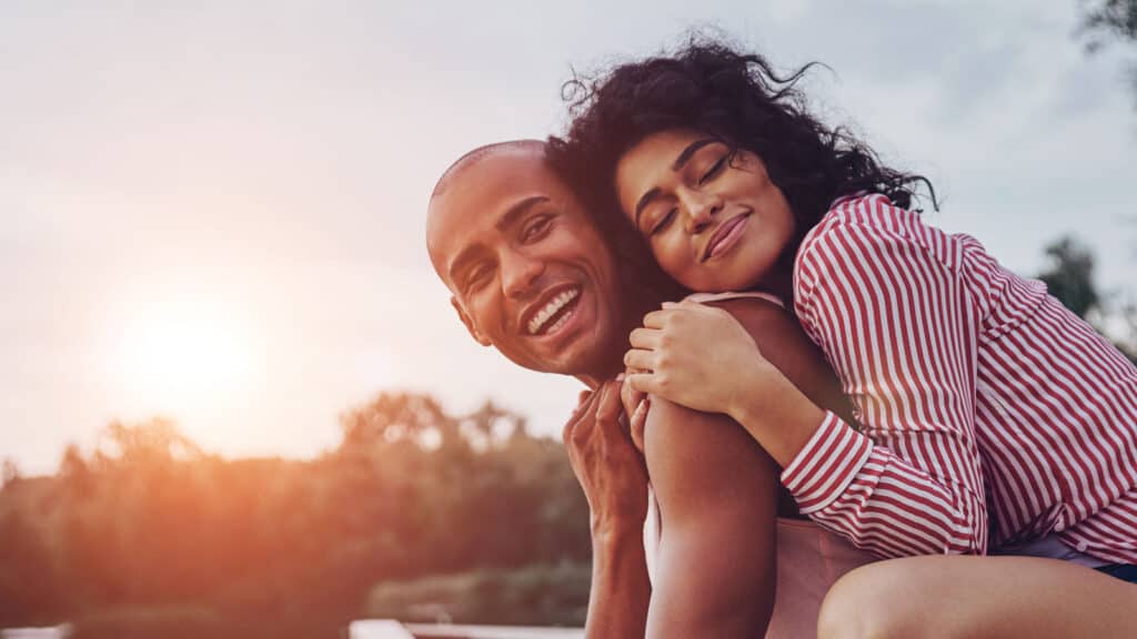 Happy moments together. Happy young couple embracing and smiling while sitting on the pier near the lake