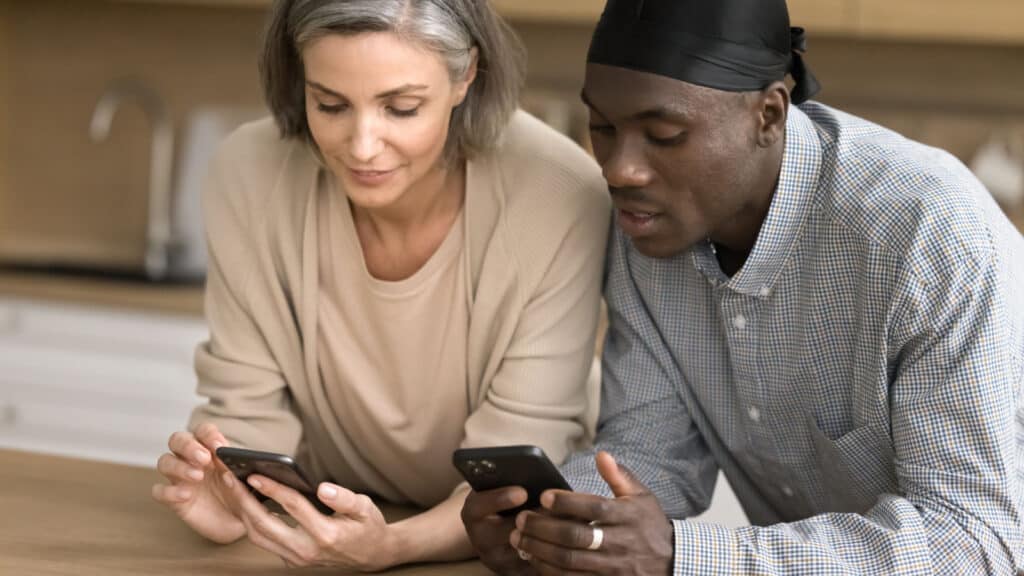 Positive middle aged multiethnic couple in love focused on smartphones, browsing Internet, discussing shopping, service, application, enjoying online communication, wireless connection technology