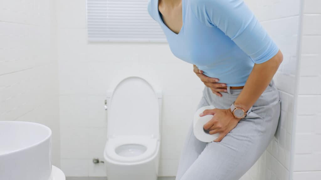 Woman clutching gut holding toilet paper.