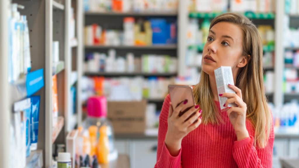 Woman comparison shopping in drugstore with phone.
