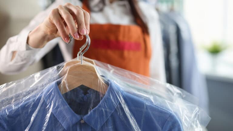 Woman holding dry cleaned shirts on hangers.