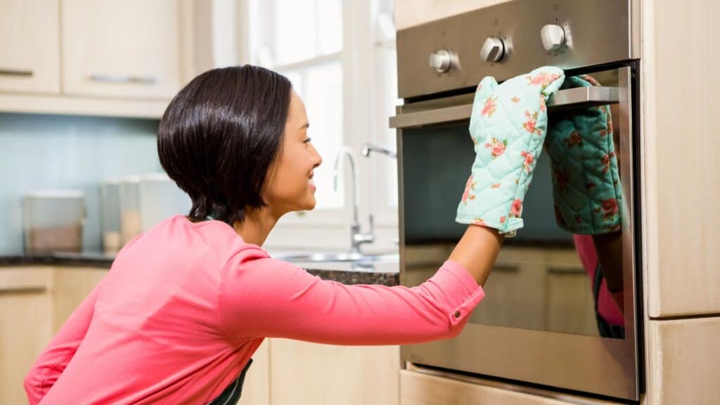 Woman looking in oven wearing oven mitt. 