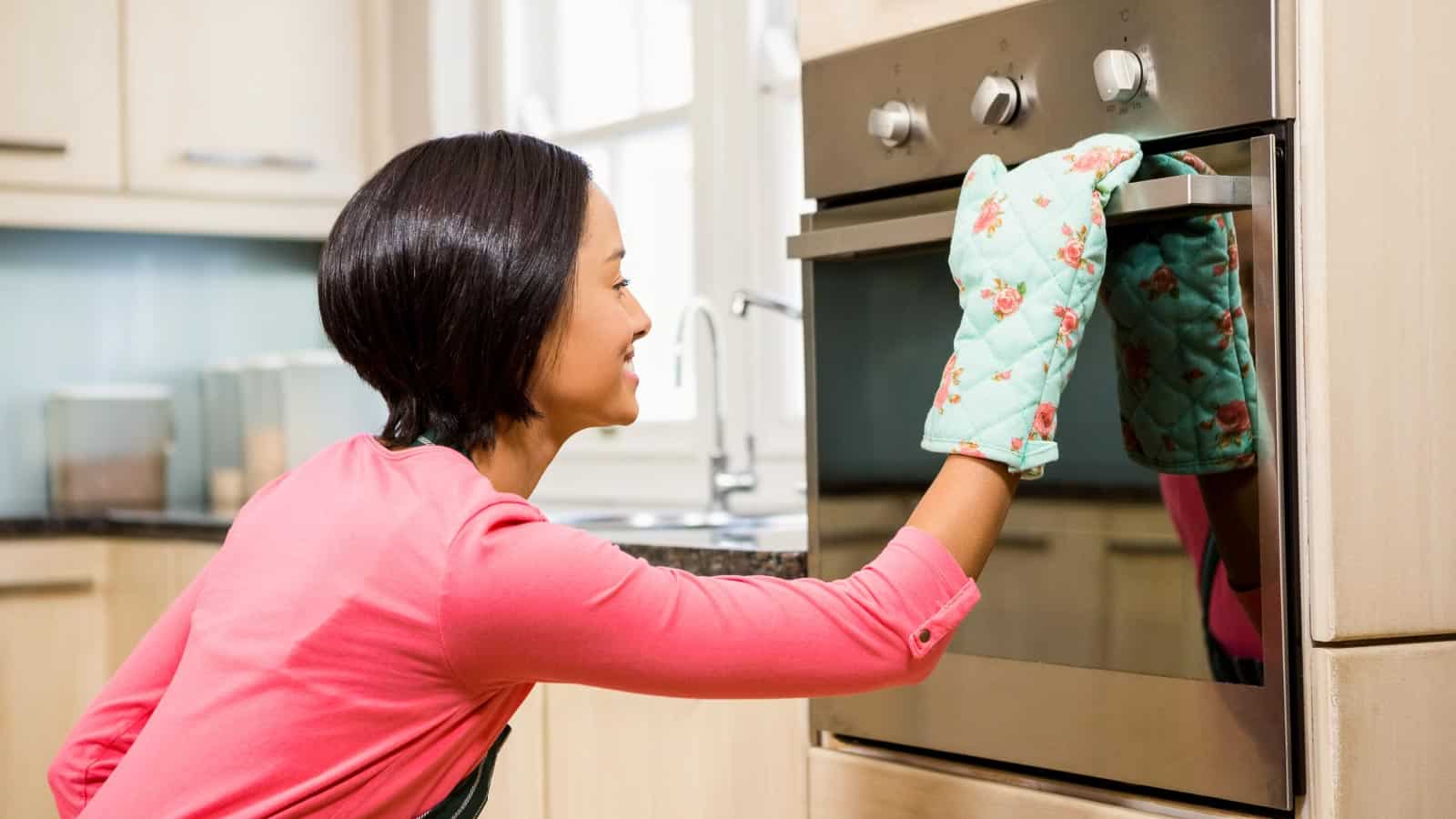 Woman looking in oven wearing oven mitt.