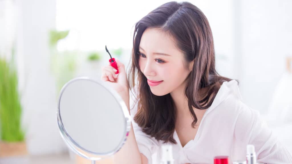 Woman using mirror to put on makeup. 