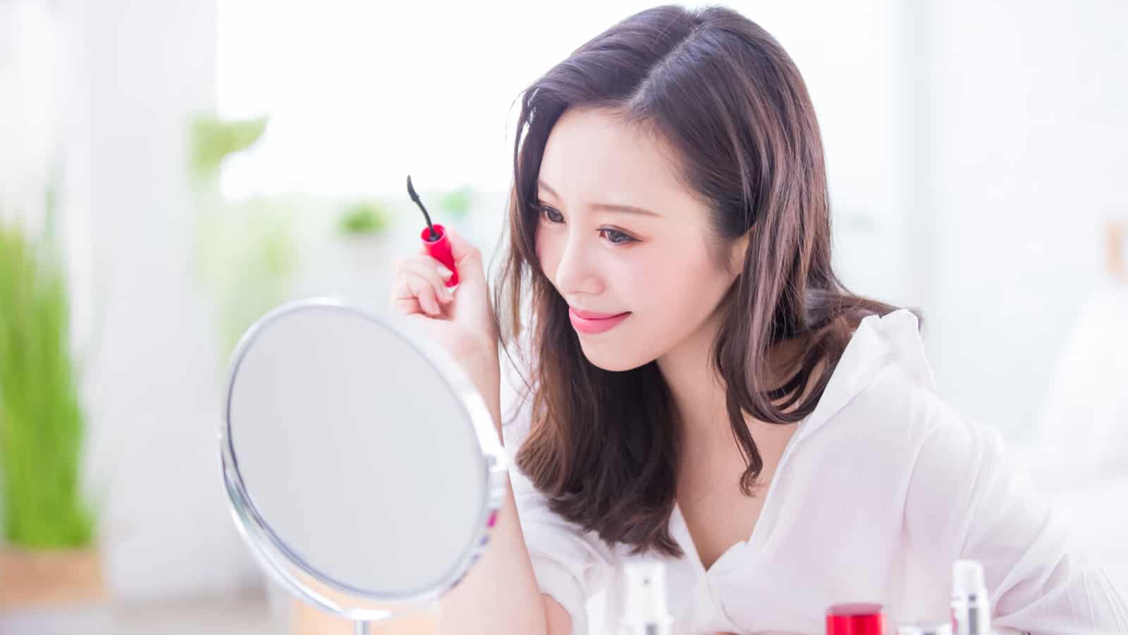 Woman using mirror to put on makeup.