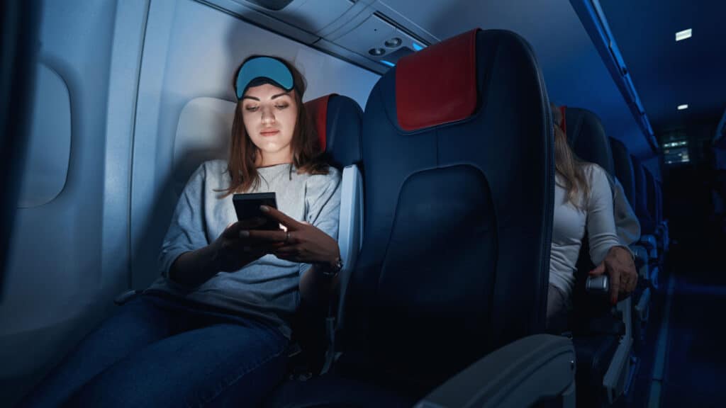 Woman using smartphone on red eye flight. Flying at night.