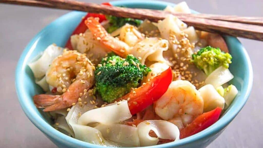 aqua-bowl-of-low-FODMAP-shrimp-and-broccoli-with-noodles-chopsticks-on-top-of-edge-of-bowl.