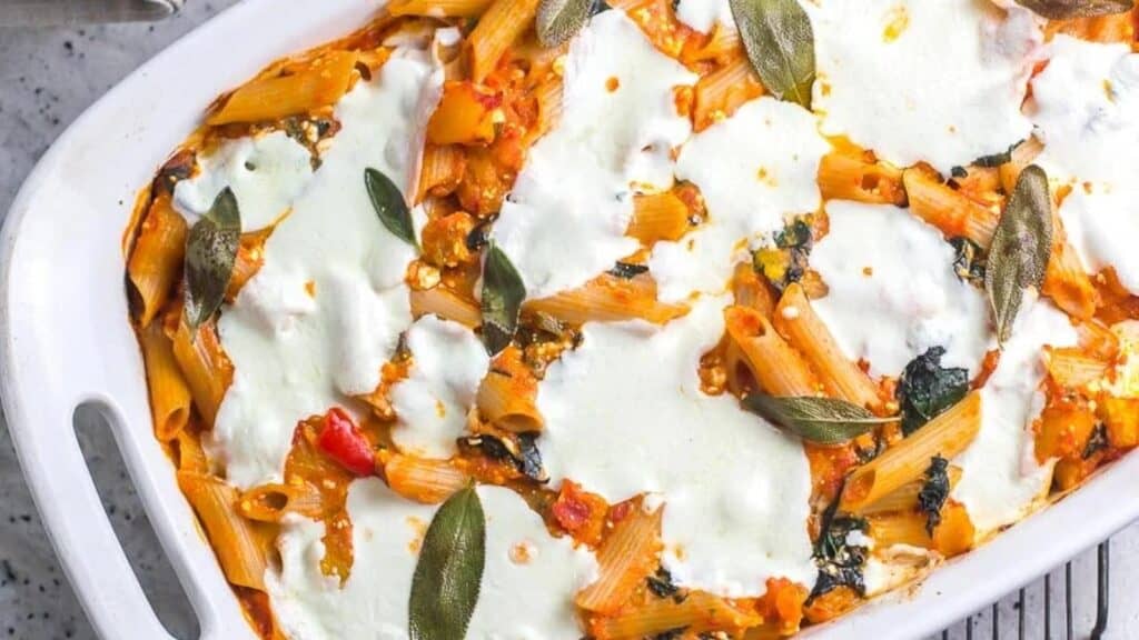 close-overhead-shot-of-baked-pasta-with-roasted-pumpkin-fresh-mozzarella-and-sage-in-white-baking-pan-on-rack.