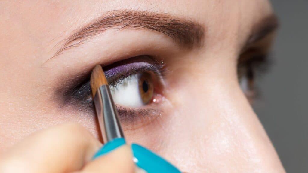 Colorful powder eyeshadow being applied to woman's eyelid.