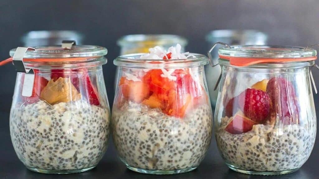 trio-of-glass-jars-holding-overnight-oats-and-chia-with-fruit-against-dark-background.