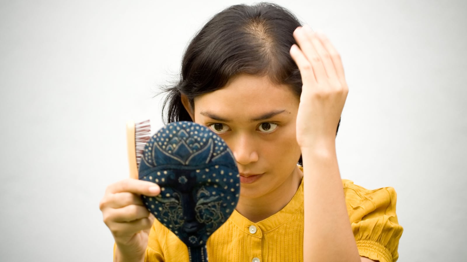 woman looking at hair loss in mirror.