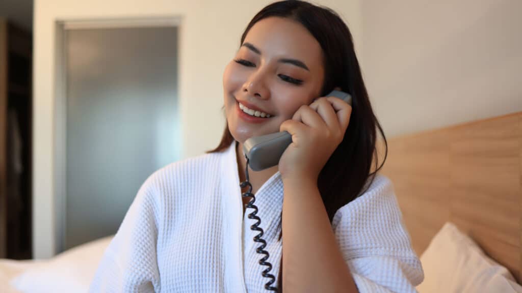 Asian woman using phone in hotel. Hotel robe.