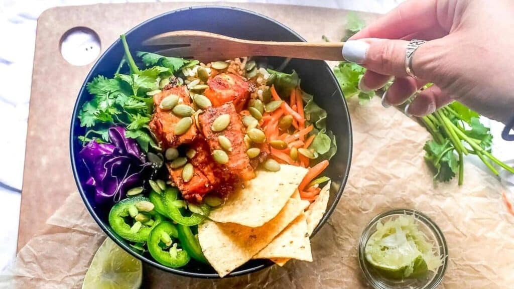 Baja-Tempeh-Taco-Salad-in-dark-bowl-womans-hand-holding-wooden-fork.