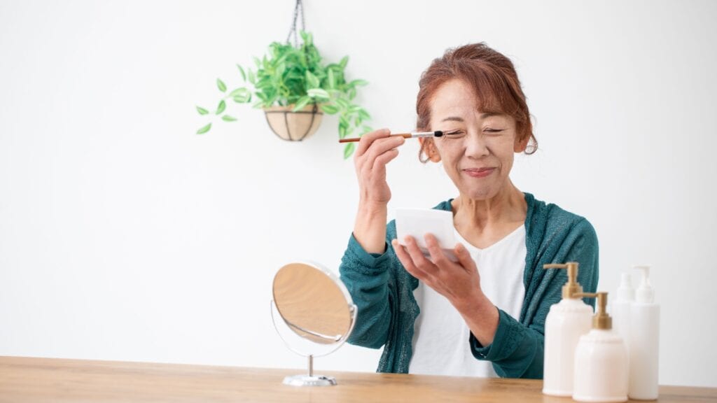 Older woman applying eye makeup. 
