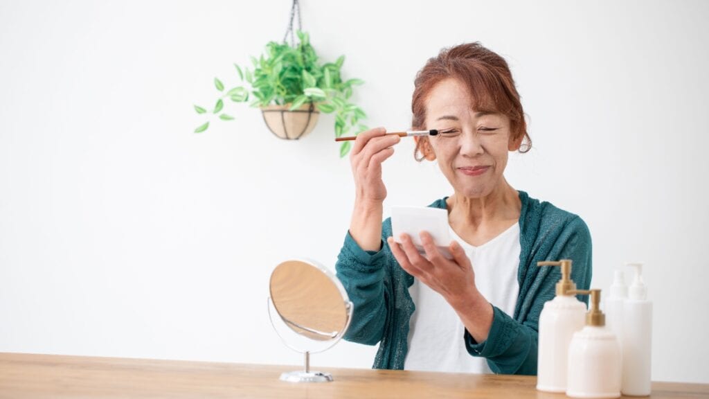 Older woman applying eye makeup.