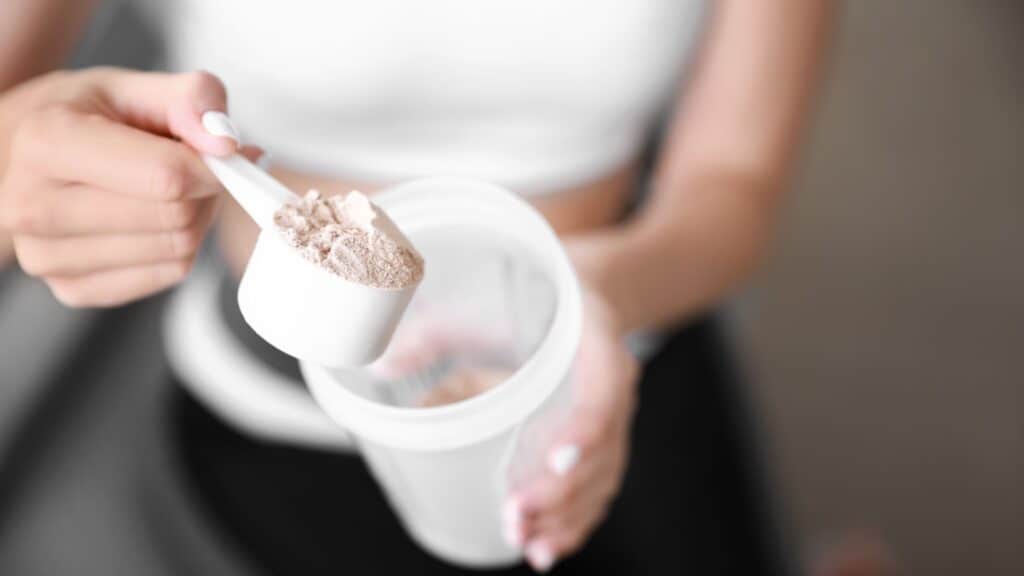 Woman scooping protein powder into container.