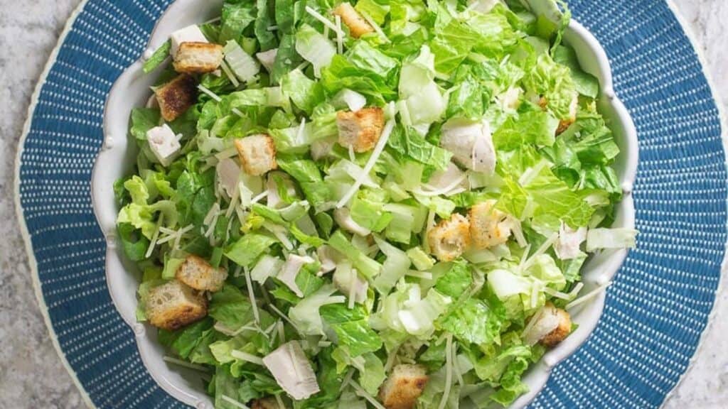 chopped-chicken-Caesar-salad-in-white-serving-bowl-on-round-blue-placemat.