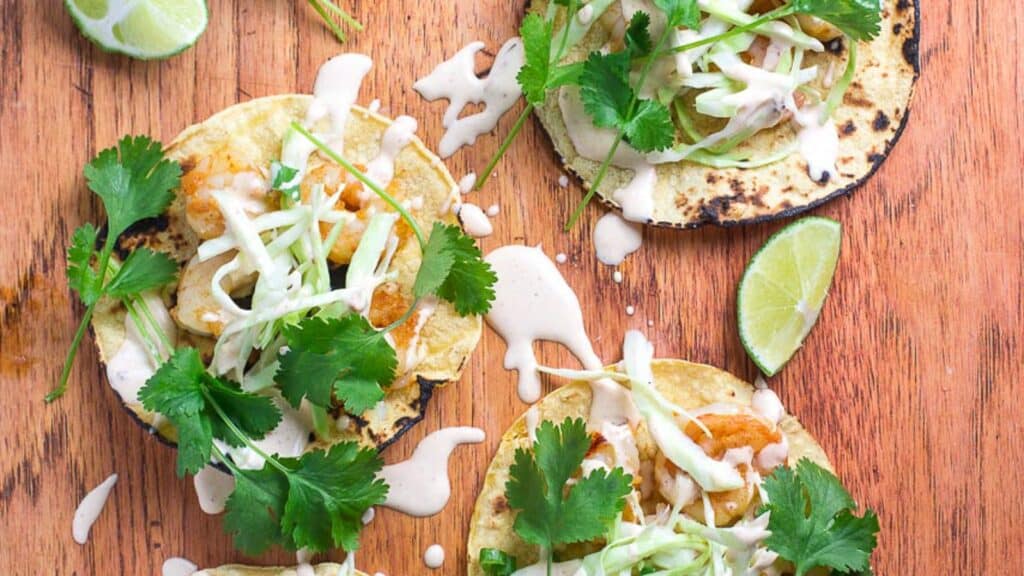 closeup-image-Low-FOMAP-Shrimp-Tacos-with-Lime-Crema-on-wooden-board-wedges-of-lime-alongside.