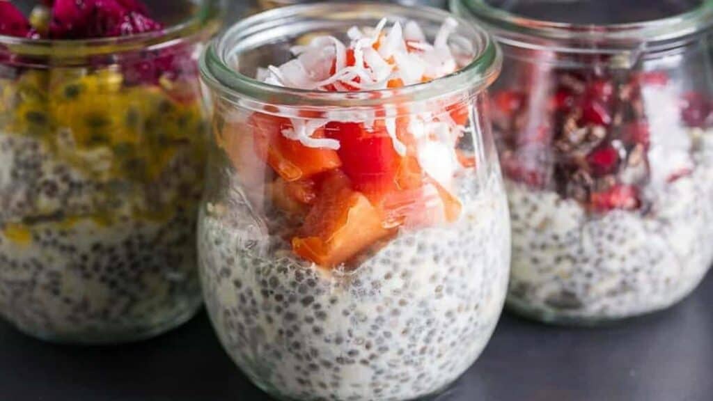 glass-jar-of-overnight-oats-and-chia-topped-with-papaya-and-coconut-against-dark-background.