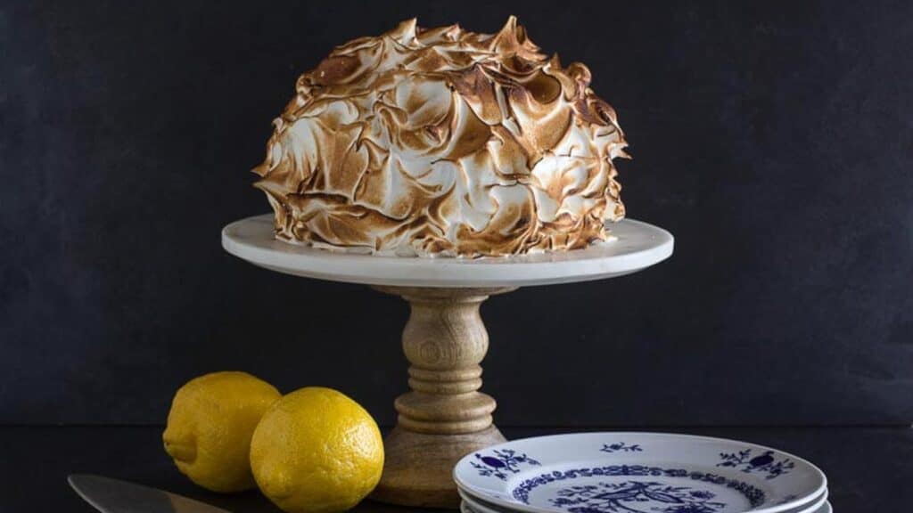 horizontal-Low-FODMAP-lemon-meringue-cake-on-white-pedestal-with-dark-background.