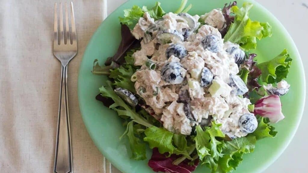 overhead-horizontal-image-of-Low-FODMAP-Chicken-Salad-with-Grapes-and-Almonds-on-a-bed-of-lettuce-on-a-green-plate-fork-and-linen-napkin-alongside.